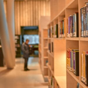 man in black jacket standing near brown wooden book shelves