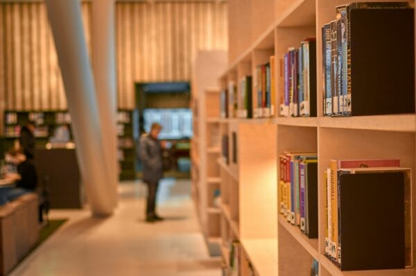 man in black jacket standing near brown wooden book shelves